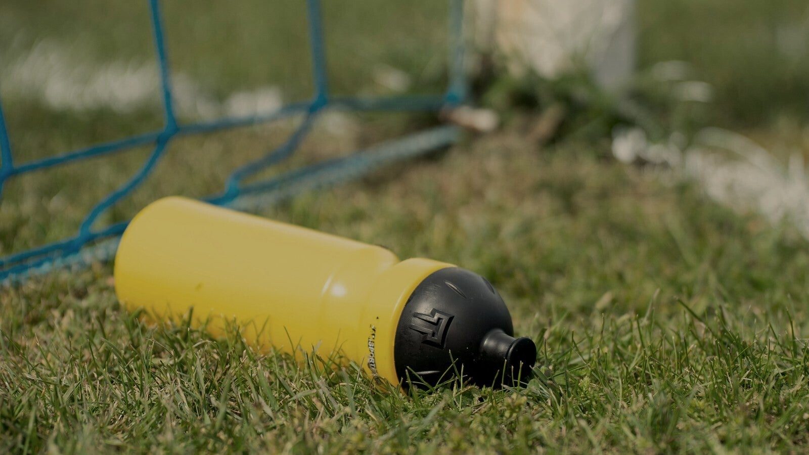 Gele drinkbus in het gras aan de voet van een voetbaldoel, hydratatie van de jonge voetballer