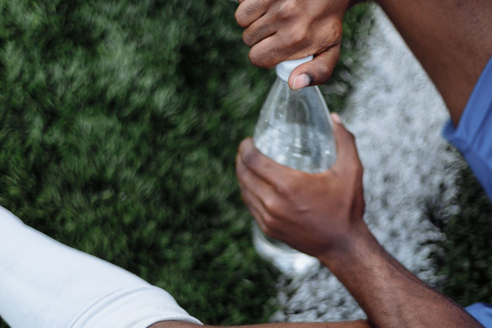 Voetballer zit op het gras met een fles water na de inspanning, het begin van het herstel na de wedstrijd